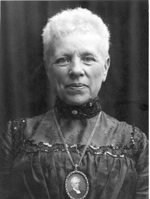 Bröstbild av prostinnan Holmberg. Hon bär ett halssmycke i form av ett mansporträtt i en oval ram - troligen hennes man, kyrkoherde Axel Alfred Holmberg.