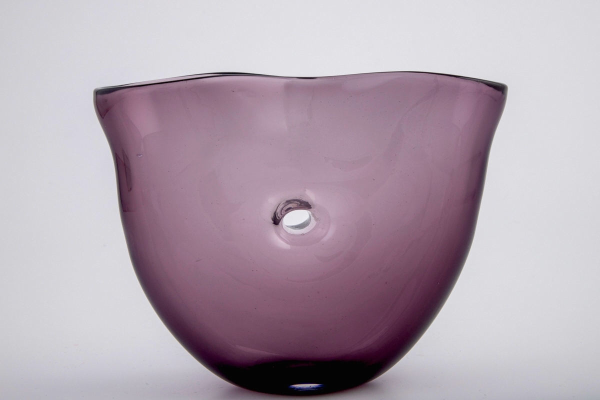 Vase i gjennomskinnelig lillafarget glass. Ovalt korpus med et gjennomgående hull i midten. Vasens munning har form av et åttetall, hvor kantene nesten møtes på midten.
