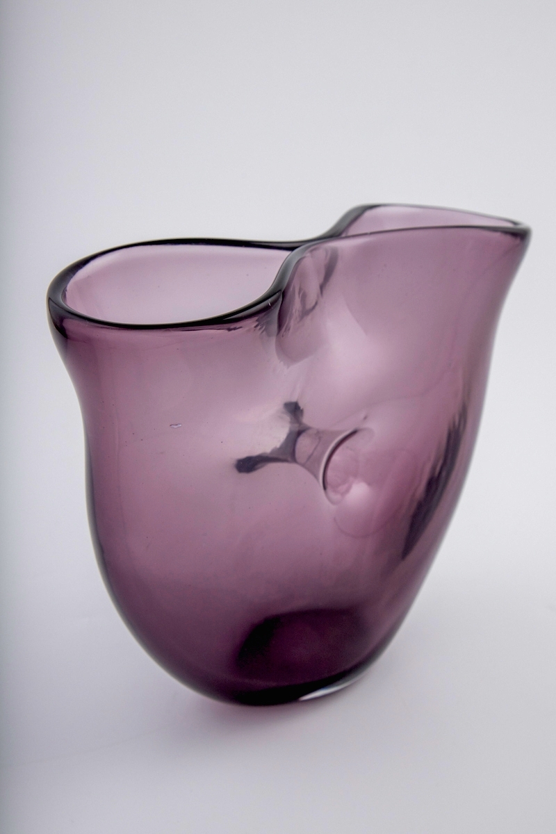 Vase i gjennomskinnelig lillafarget glass. Ovalt korpus med et gjennomgående hull i midten. Vasens munning har form av et åttetall, hvor kantene nesten møtes på midten.