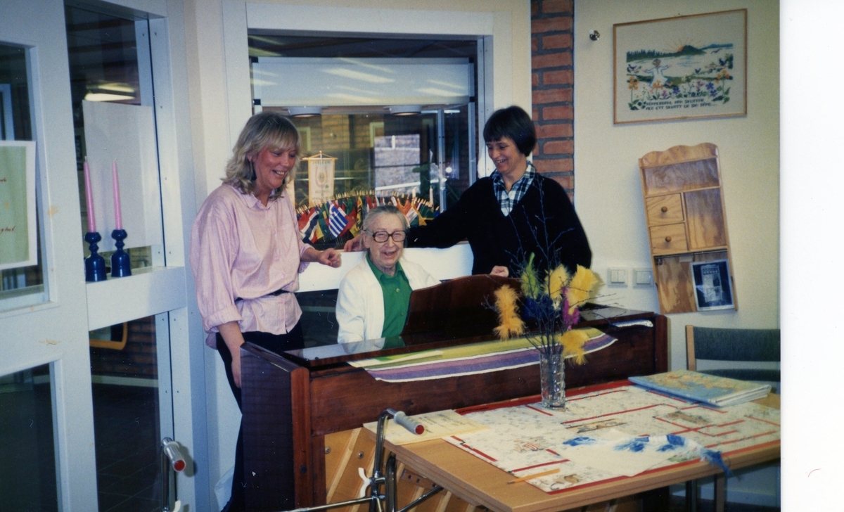 Musikunderhållning i Brattåsgårdens hobbylokal på Våmmedalsvägen 1980-tal. Från vänster ses vårdbiträde Susanne Olsen, vid pianot (tidigare pianolärare) Marianne Skarin (1906 - 1991) och vårdbiträde Anna-Lisa.