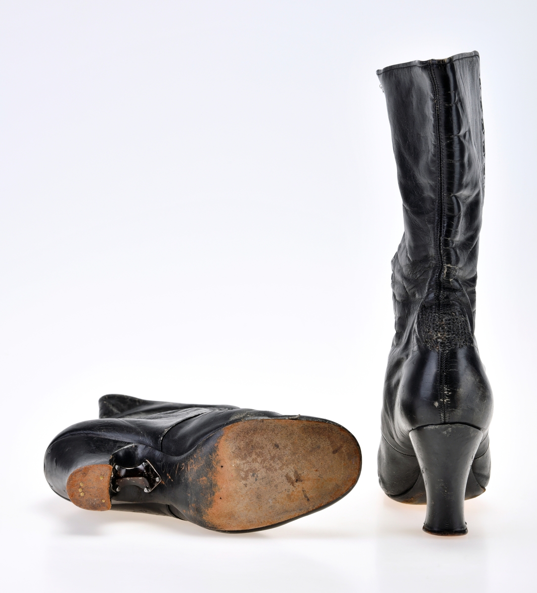 Et par damesko/støvletter av svart skinn. Skoene er avrundet foran. I front er det 19 par hull/maljer for snøring. Skoene mangler skolisser. Under snøringen er det en enkel skinntunge foret med hvitt lerretsstoff. Skoene er foret med hvitt lerretsstoff, øverste 7cm er blått lerretsstoff. Innersålen er av brunt skinn. Yttersålen og hælen er av svart lær som er nedslitt. Mellom hæl og såle er det satt på et metallbeslag (stiftet på). Støvlene har høye hæler.