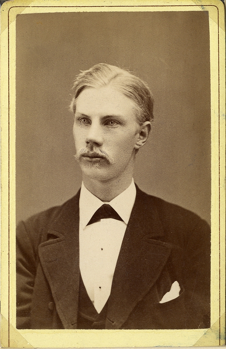 Porträttfoto av en ung man i kavajkostym med väst, stärkkrage och fluga. 
Bröstbild, halvprofil. Ateljéfoto.
