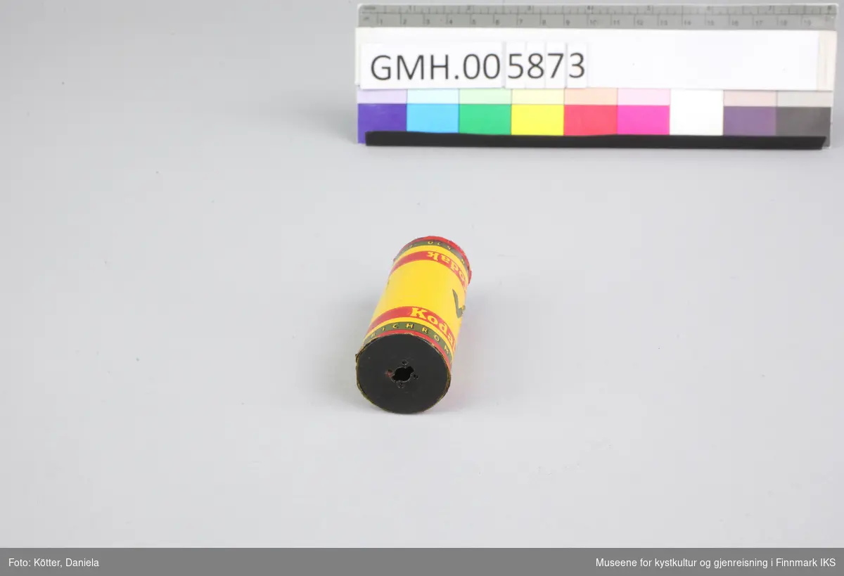 Dette er en filmrull på en metallspole. Selve filmmaterialet beskyttes av papir i gult, rødt og svart. Filmen er ubrukt.