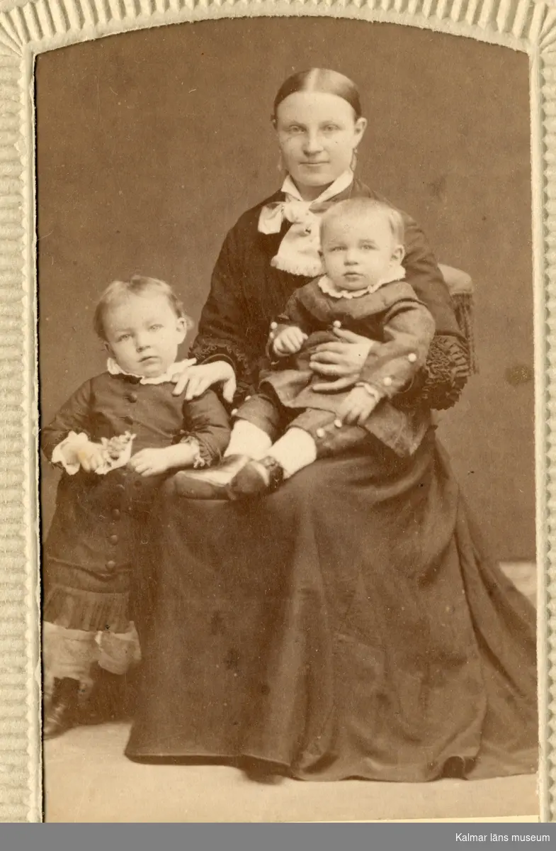 Porträtt av Anna Charlotta Petersson, klädd i mörk klänning, med två av sina barn.