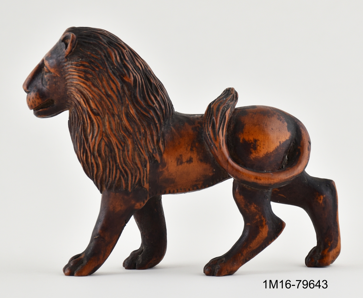 Figurin, lejon, skuret i trä, stående med svansen över ryggen.