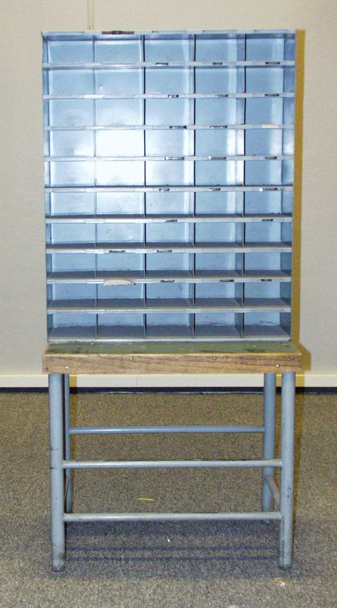 Blå sorteringshylle i metall. Den har bordplate av tre under, og benene er lagd av metall.