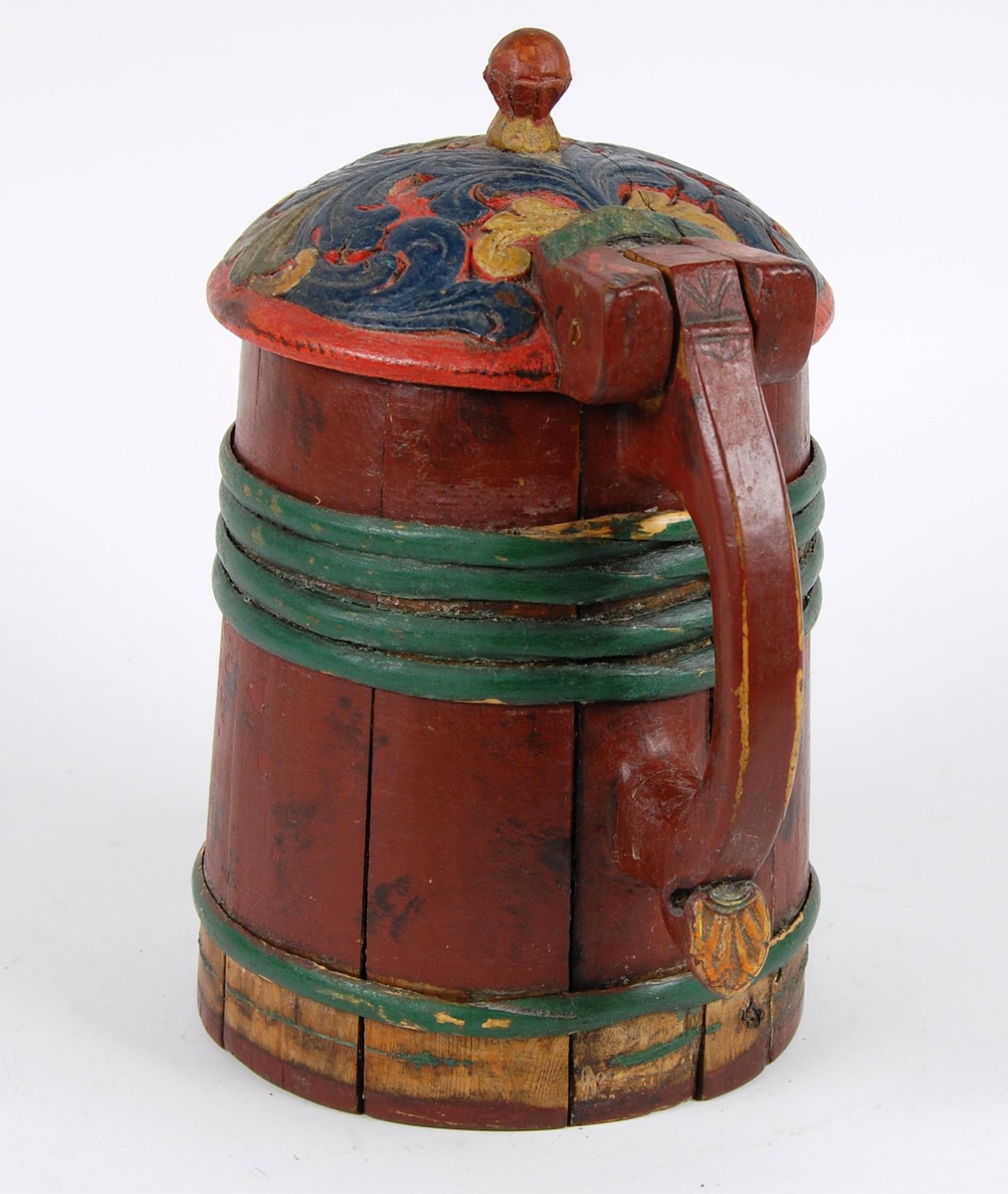 Kanne av furustaver. Lokk med akantusskurd malt i grønne, gule og blåe farger. Kuleformet lokkgrep. Korpus med fire grønnmalte gjorder oppe og en nede (opprinnelig tre). Hanken er utskåret av en av stavene, ender nederst i en plate med bladmotiver.