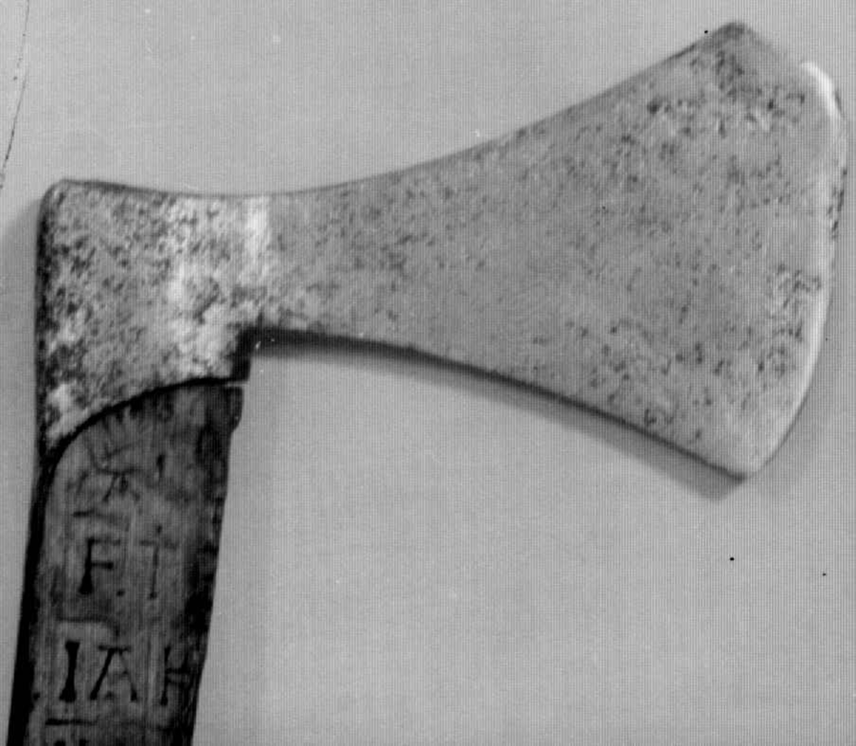 Asymmetrisk økseblad, sammensveiset med overliggende jernskinne.
Fremre øksebladspiss brukket.
Rikt dekorert skaft med flettet rutemotiv. Innskripsjon på øvre del av skaftet (se Påført tekst)
