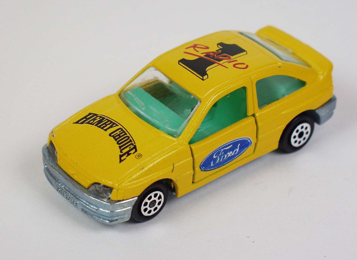 Gul lekebil av hard plast og metall. Bilen har reklame for Radio 1 og Henry Choice.
