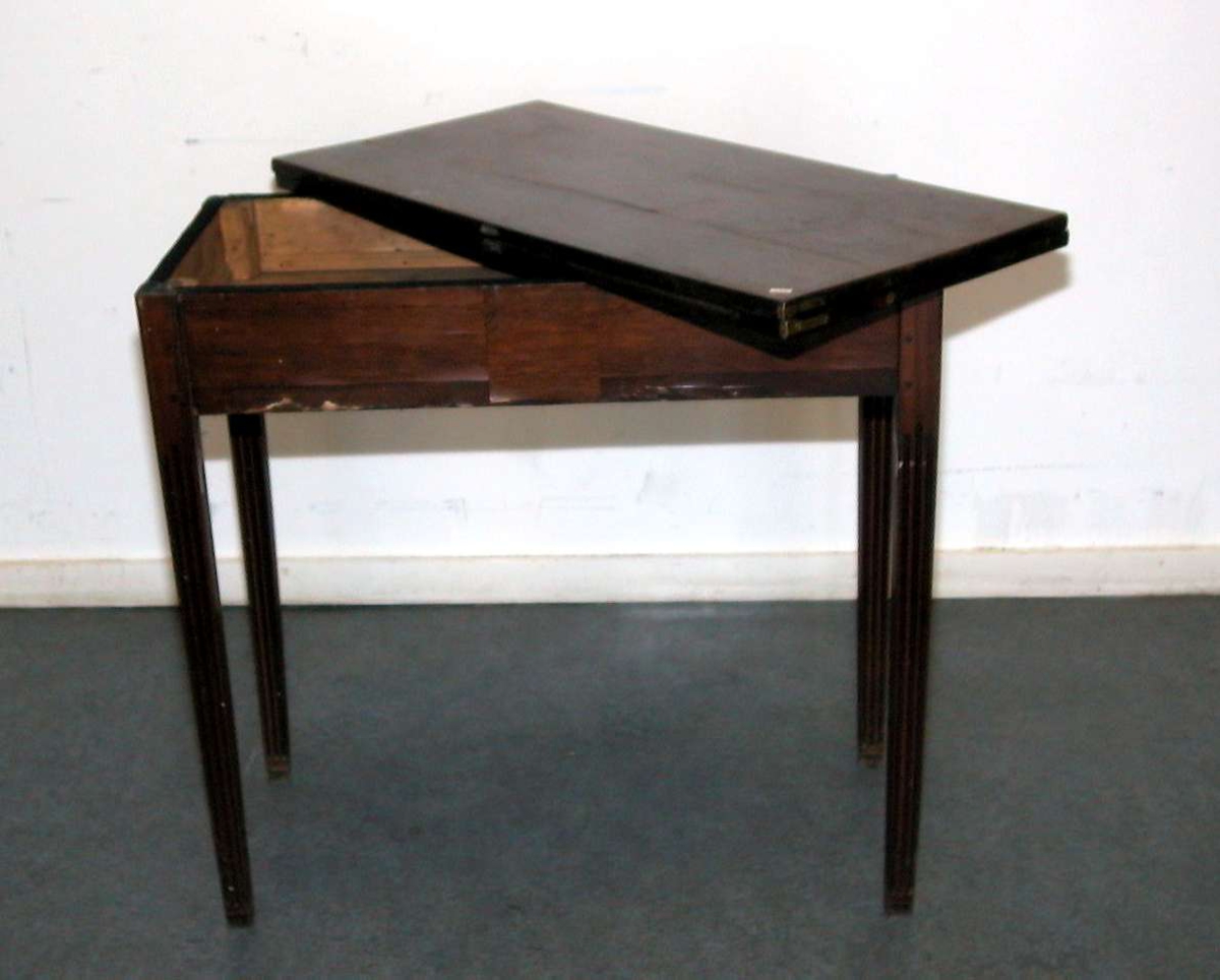 Spillebord med utslagbar plate. Det er et rom under bordplaten. Platen har fire fordypninger. Bordet har rette ben med rifler. Fineringen på en side av sargen er skadet. Bordet er brunpolert.
