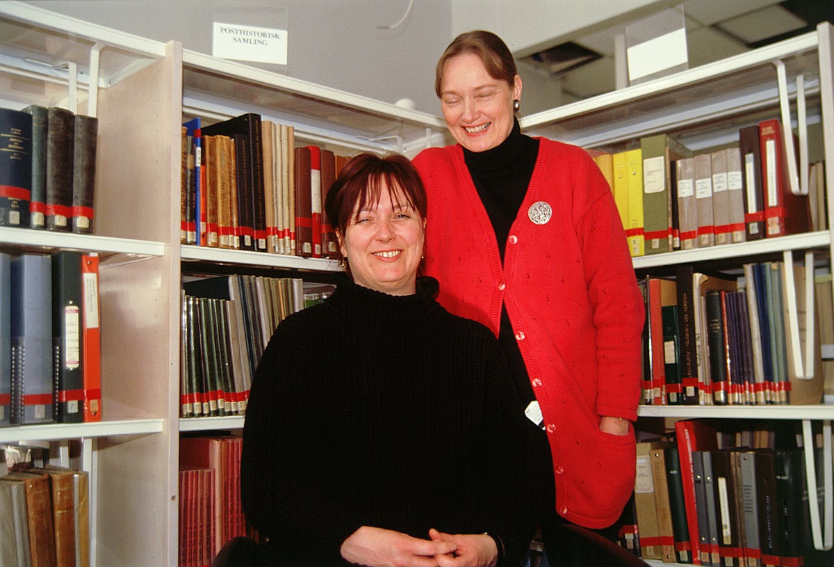 postmuseet, Kirkegata 20, biblioteket, Elin Eskerud sitter og Torgunn Haugaard står foran bokhyllene