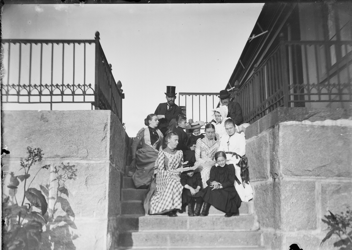 En gruppe mennesker sitter i trappa på Linderud Gård i sterk motsol.