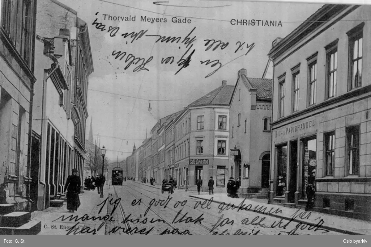 Nedre del av Thorvald Meyers gate med trikk, hestekjerre og spaserende. Butikk, café, butikkskilt. Postkort med påskrevet hilsen. datering etter 1891 (jf. tårnet Paulus kirke i bakgrunnen)