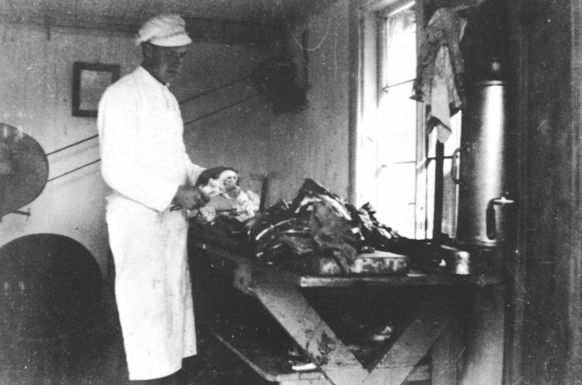 Interiør, slakteri, slakter Ole Pram skjærer kjøtt. Slakter Barflo leide et lite hus bak Framheim kino av fiskehandler Hermansen. Brumunddal.
