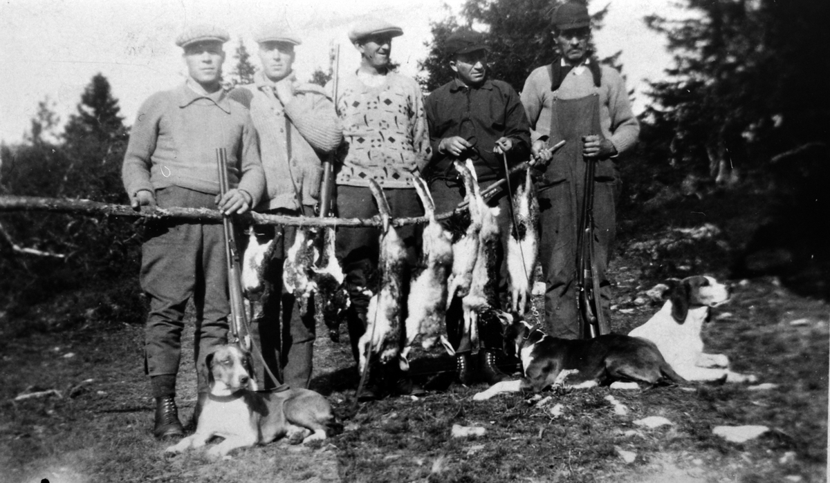 Fem personer på jakt. Til venstre er Aksel Johansen, i midten er Hans O. Houmb, til høyre er Alfred Thoresen, de andre er ukjente. Hunder og jaktutbytte.
