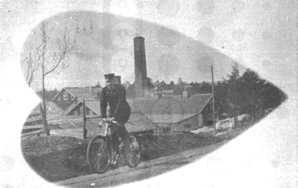 Eldre mann i uniform(?) på sykkel opp gamlevegen til Aadals Brug/Klevbakken. Klevfos Cellulose og papirfabrikk ligger nedenfor, slik bygningene så ut før brannen i 1909. (Gjenoppbygd i 1911) Løten. Ådalsbruk.