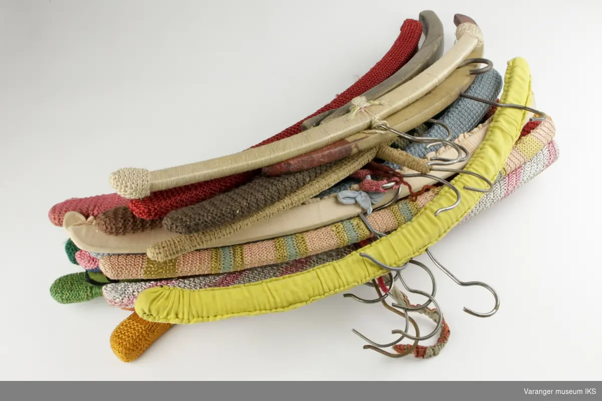 Samling av kleshengere, 20 stk. Av disse er 18 kledd i en eller annen form for tekstil, enten strikk, stoff, tråder eller en kombinasjon av disse teknikkene.