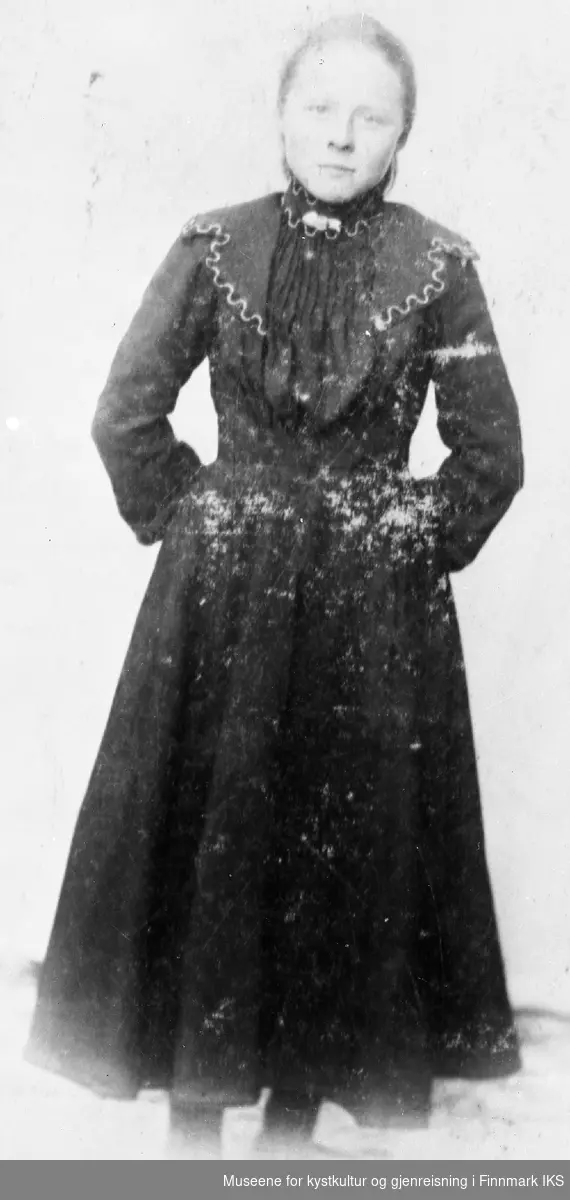 Jenny Jakobsen i konfirmasjonskjole. Kjolen har stor krav og høy hals. Det er en spenne oppe i halsen. 1905
