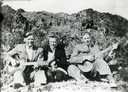 To menn og en kvinne sitter i en bakkeskråning og spiller på