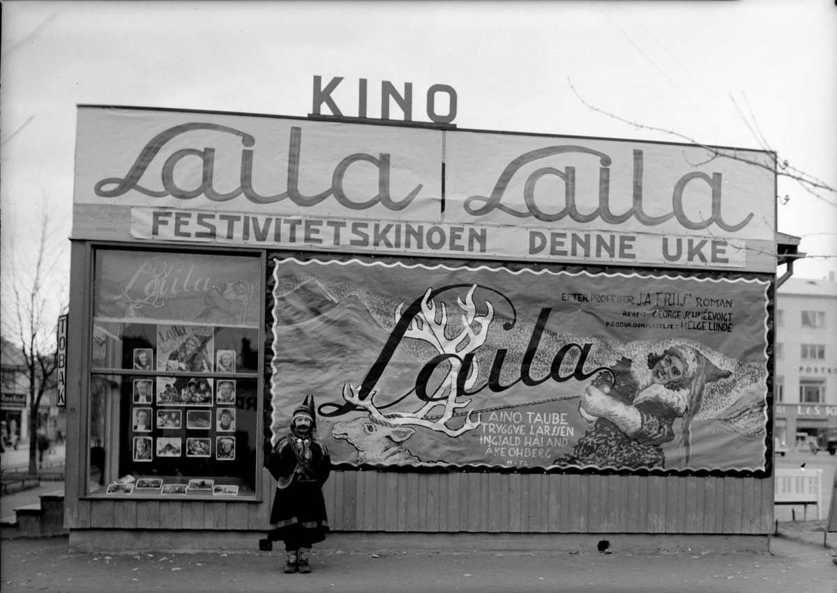 Kinoreklame på Østre Torg for relanseringen av filmen "Laila" som skulle vises på Festiviteten Kino. For å skape litt publisitet rundt filmen fikk kinosjef Hans Smørsten unggutten Alfred Sakrisvold til å kle seg ut som en av rollefigurene. 

Disse brakkene ble satt opp etter brannen i posthuskvartalet i 1935 slik at butikkeierne kunne fortsette med sin forretningsdrift. 