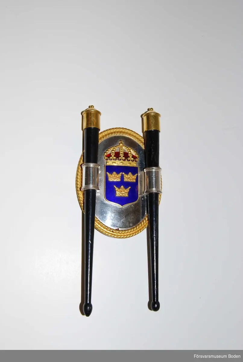 Trumpinnar med hållare monterad på sköld med blåemaljerat tre kronor-tecken.