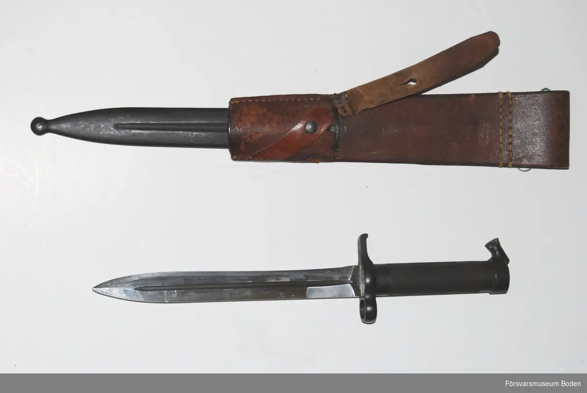 Kort knivbajonett med stålfäste och eneggad klinga avsedd för gevär m/1896. Konisk låsknapp. Med bäranordning av lång modell med två slejfar samt stålbalja. Bäranordningen har stämpel från Norrbottens regemente I 19, Boden.