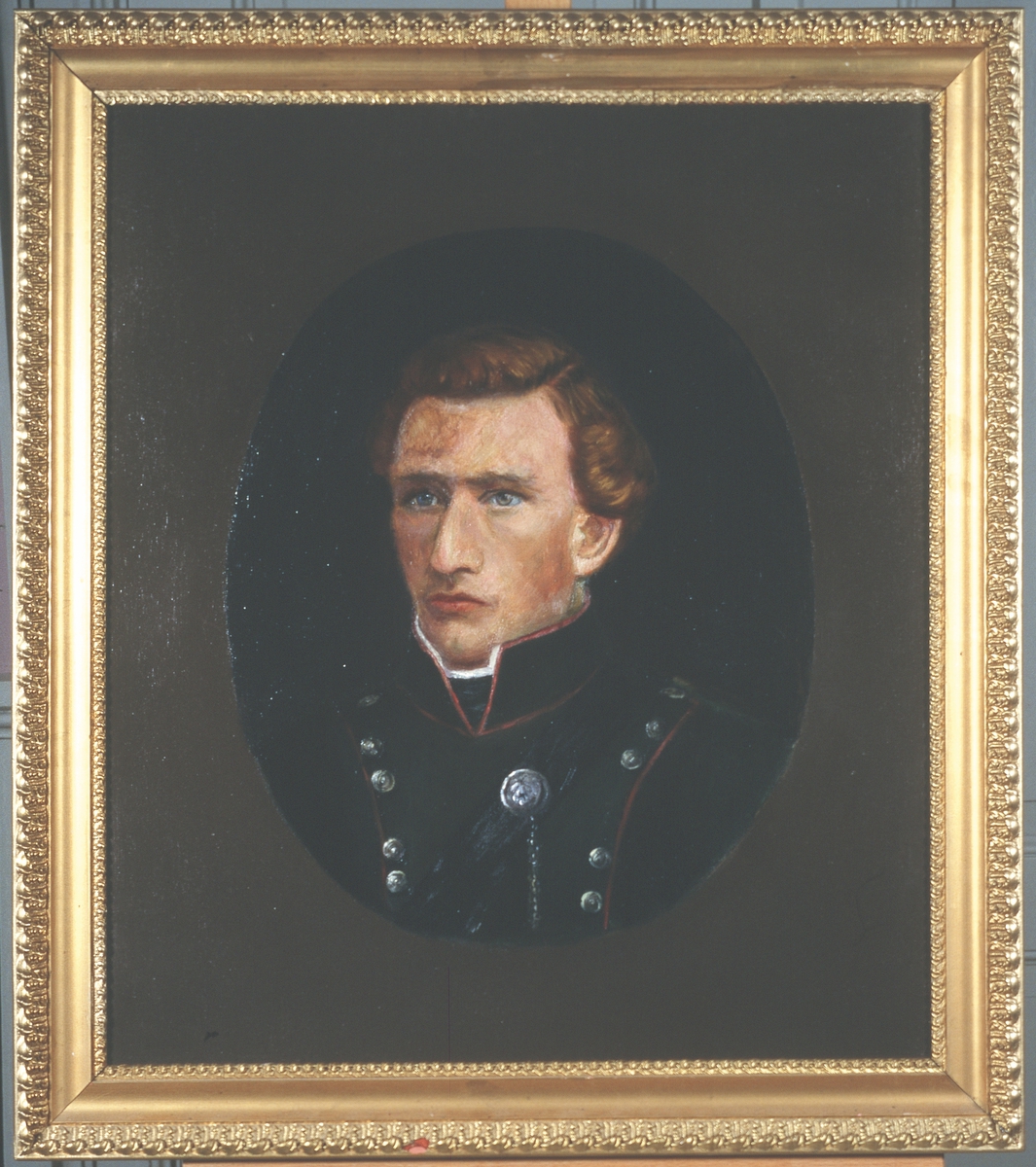 Portrett av eidsvollsmann Peter Johnsen Ertzgård
Mann innskrevet i oval, på lysere bunn
Brunt hår, uniform med smale, røde kanter, mange knapper.