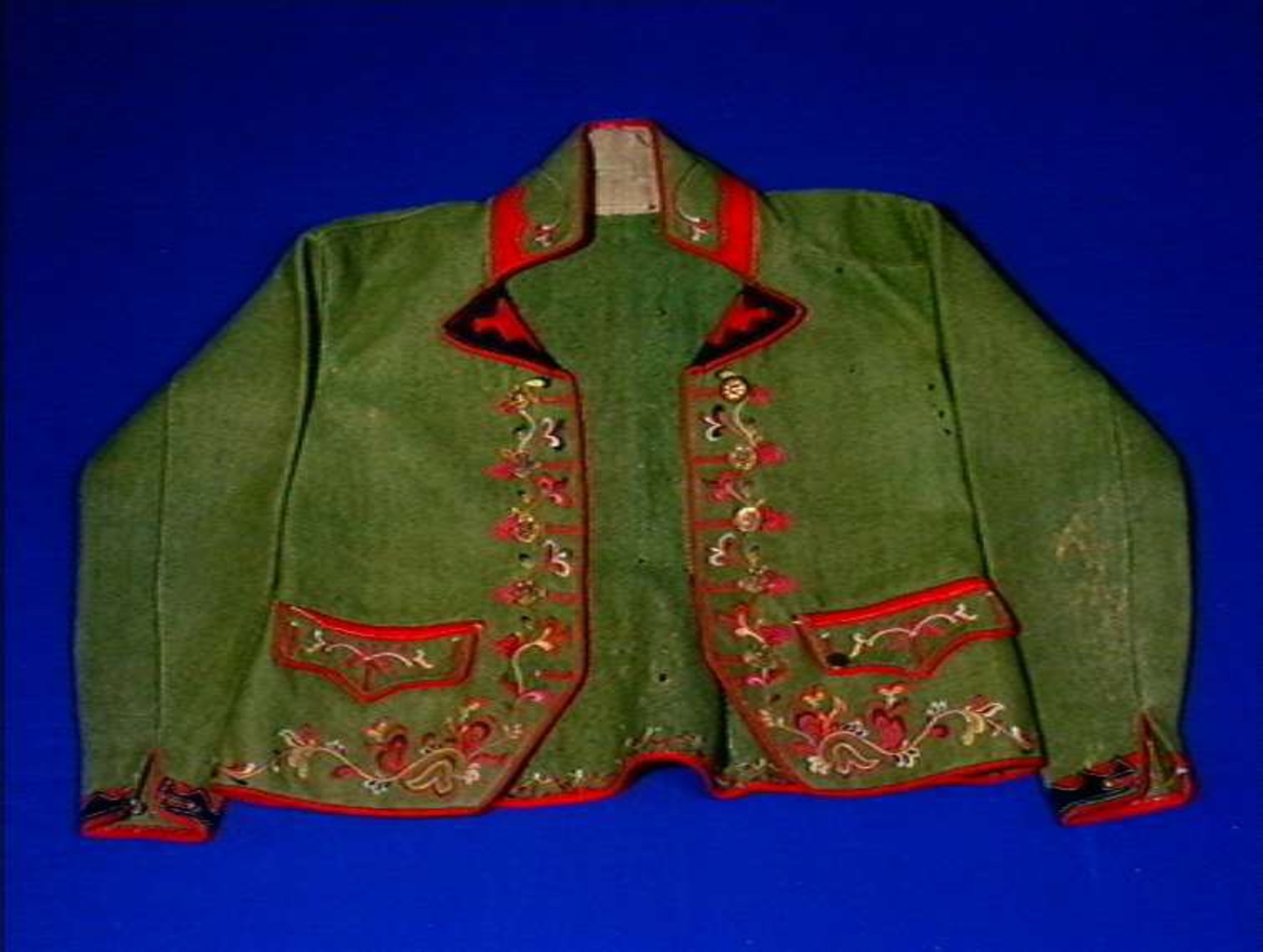 Grønn trøye med flerfarget ullgarns broderi som dekor og rød kanting.