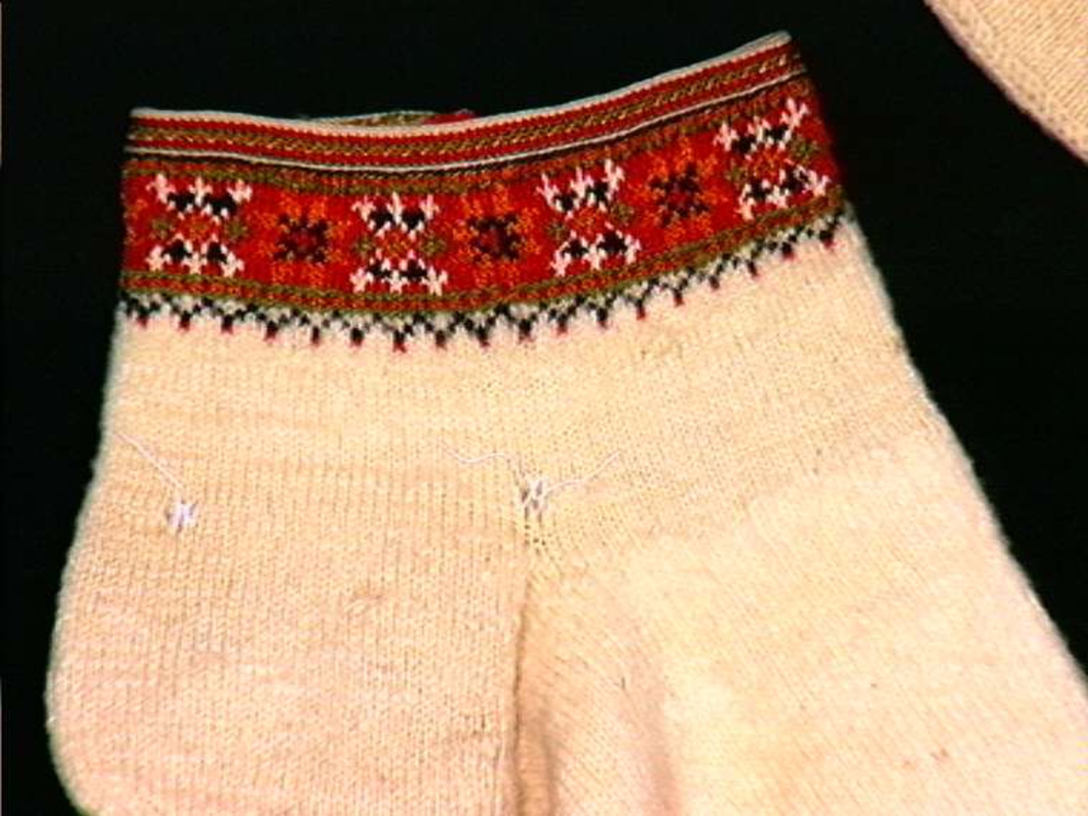 Hvit sokk med flerfatget strikket mønsterbord langs overkanten.