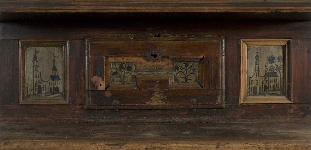 Framskap i en del med en dør nede, en  oppe og en liggende i midten. Dørene har malte blomstermotiver mens de 8 sidefeltene har malte bygninger.