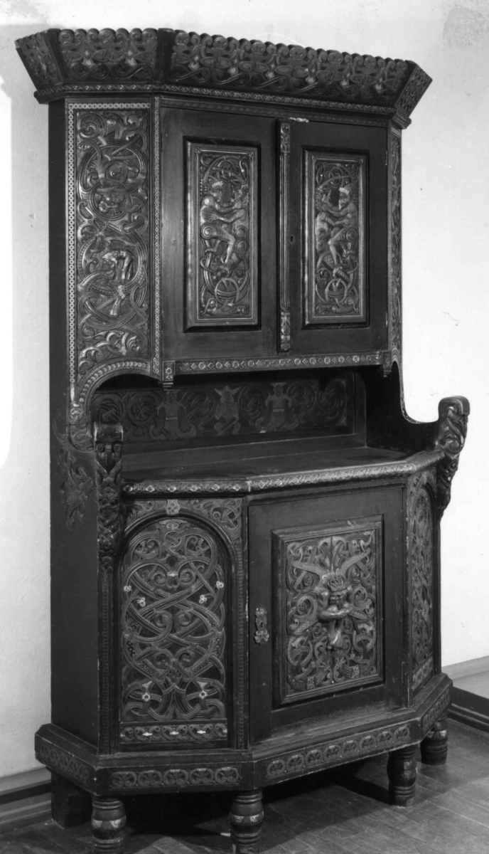 Skåret av treskjæreren Lars Kinsarvik (1846-1925), som utviklet sin særegne variant av drakestilen. Kinsarvik drev egen treskjærerskole, og var fra slutten av 1880-årene lærer ved Kristiania Kunstindustrimuseum.