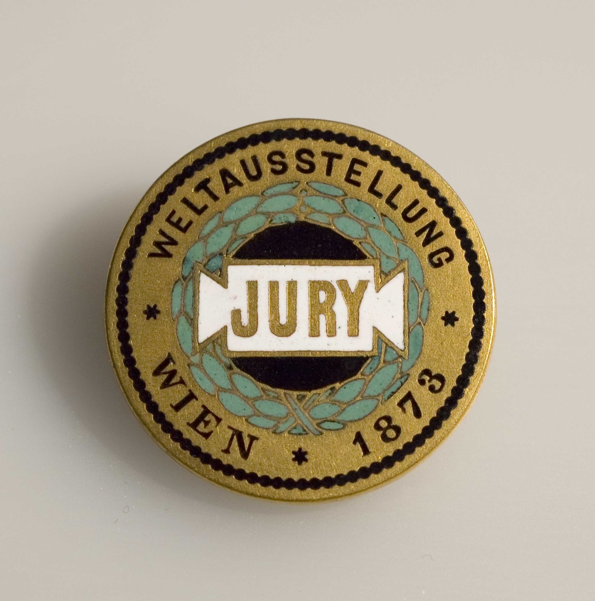 Oppstillingsliste: " Juryknapp / Metall med trykk / Innskrift: Weltausstellung Wien 1873."

