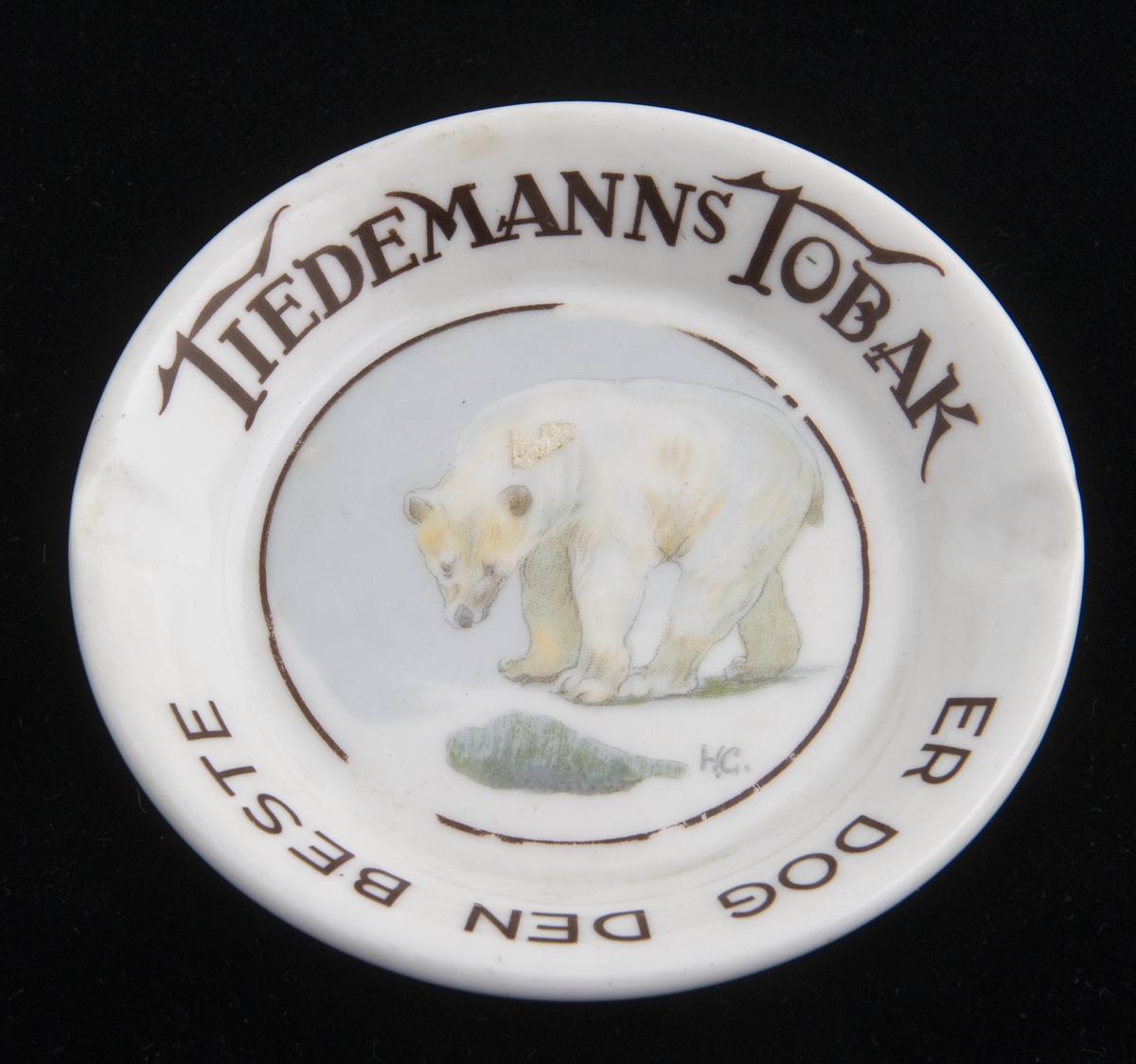 Lite, rundt askebeger i porselen med to fordypninger i randen. Påtrykket motiv av en isbjørn etter original av Halfdan Gran.