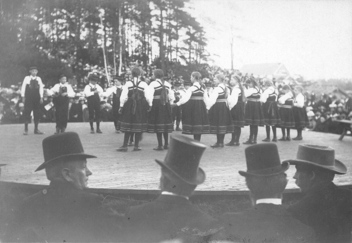 Høstfest på Norsk Folkemuseum i 1902. Folkedansgruppe på Leikarvollen. Publikum med hatter og flosshatter i forgrunnen.