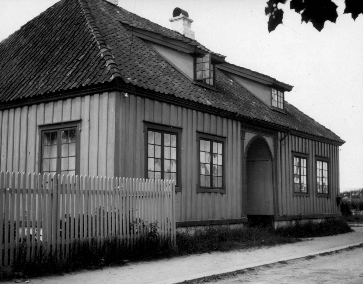 Den gamle Tollbod, Tollbodgaten 1, Porsgrunn. Huset ble i 1970 flyttet til Porsgrunn Bymuseum. Postkort. Trehus med valmet tak, portal inn til huset.  Stakittgjerde mellom hage og vei.