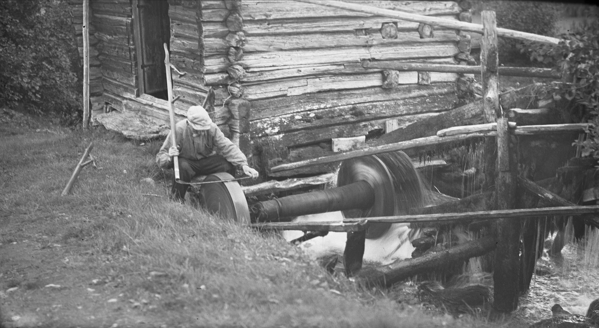 Sliping av ljå på slipestein drevet med vannkraft, Vognill, Oppdal, Sør-Trøndelag. Fotografert 1936. 