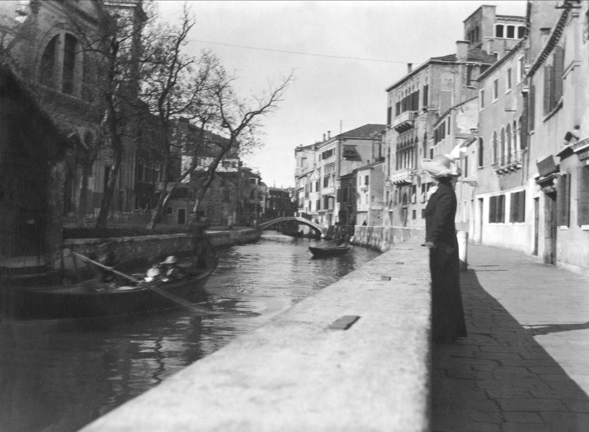 En kvinne står å ser på gondoler på en kanal i Venezia. Robsahm og Lund.