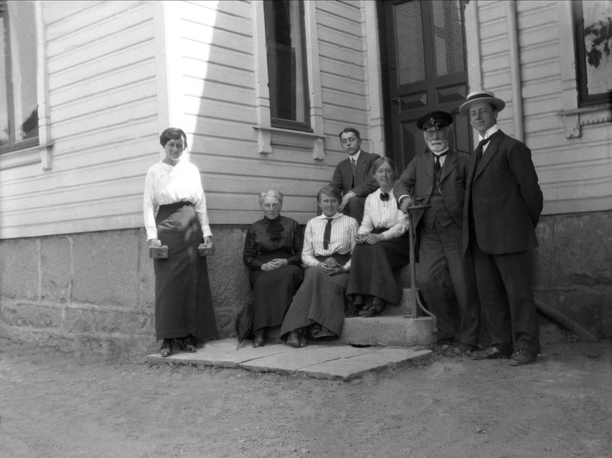 En gruppe mennesker står oppstilt i en trapp ved en inngangsdør. Robsahm og Lund.