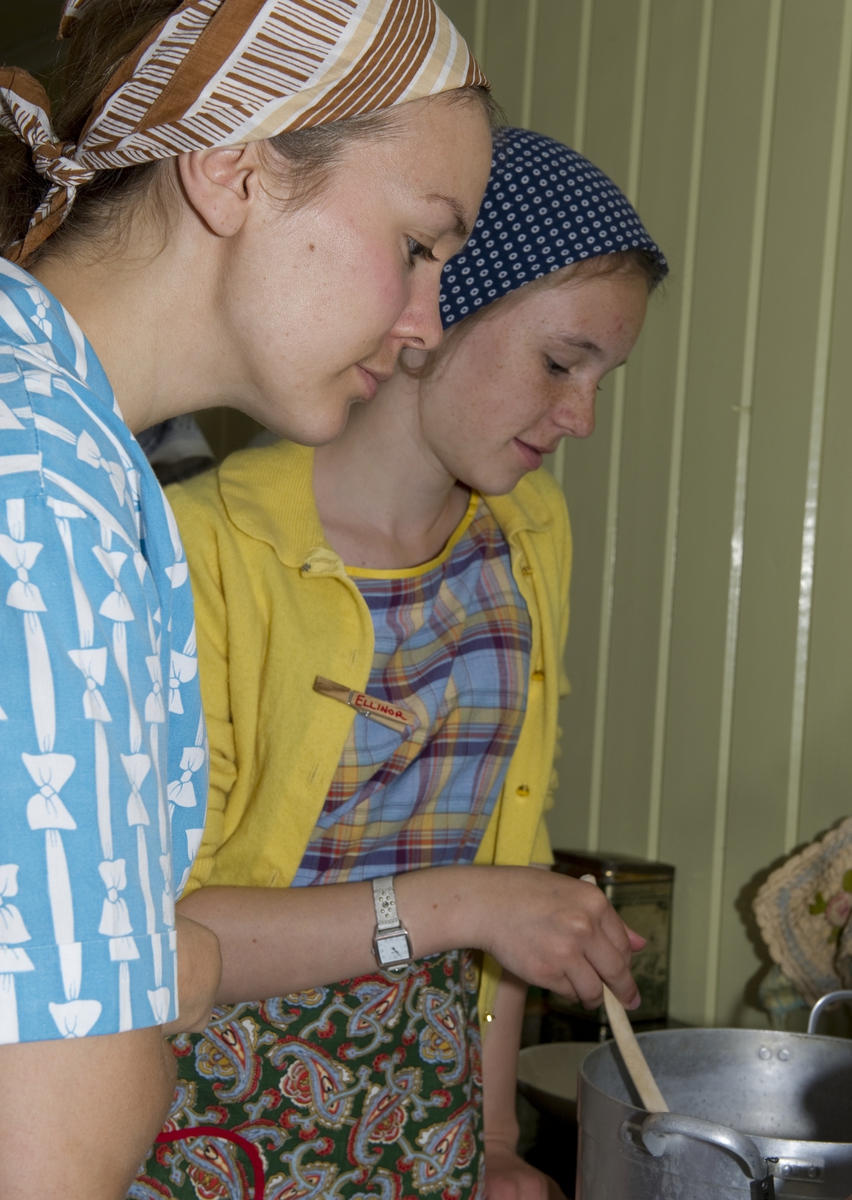 To jenter lager mat på kjøkkenet. Trønderskolen anno 1959. Norsk Folkemuseums sommertilbud til ungdom. Deltakerne prøver seg på praktiske arbeidsoppgaver som det var vanlig at ungdom deltok på for 50 år siden. Trøndelagstunet på Norsk Folkemuseum, 1. august 2012.