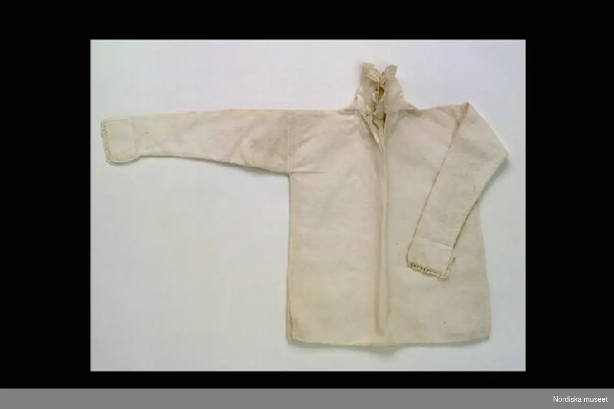 Inventering Sesam 1996-1999:
L 23 cm
Skjorta till docka av vit bomull, sprund i sidorna, lång ärm, knypplad spets i ärmslut och på kragen.
Helena Carlssson 1997