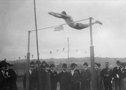 Stavhopper i svevet over stanga. Tilskuere i uniform og helg