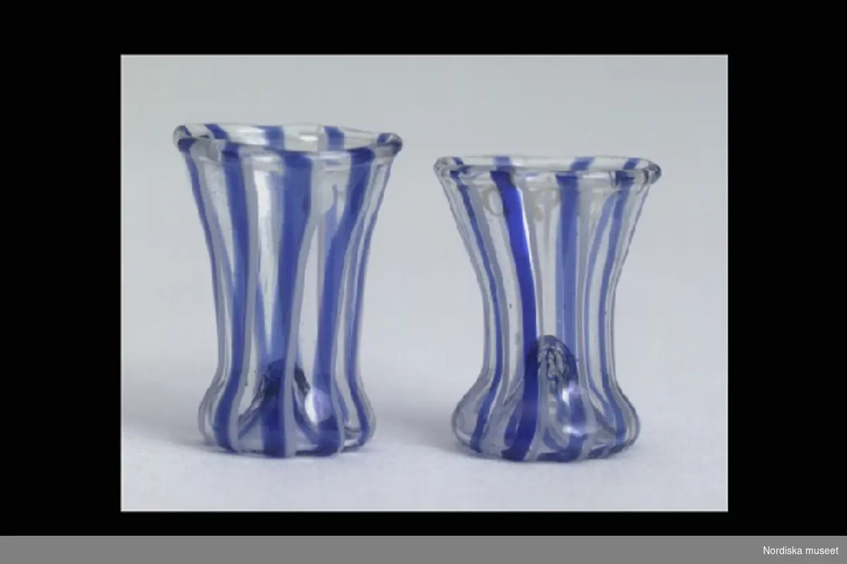 Inventering Sesam 1996-1999:
H 1,5 cm (glasen)
Vattenkaraffin och två dricksglas med utsvängdform, blå och vit randiga. 
Tillhör dockskåp inv 200.513.
Vid inventering 1996 saknades karaffen.
Birgitta Martinius 1996