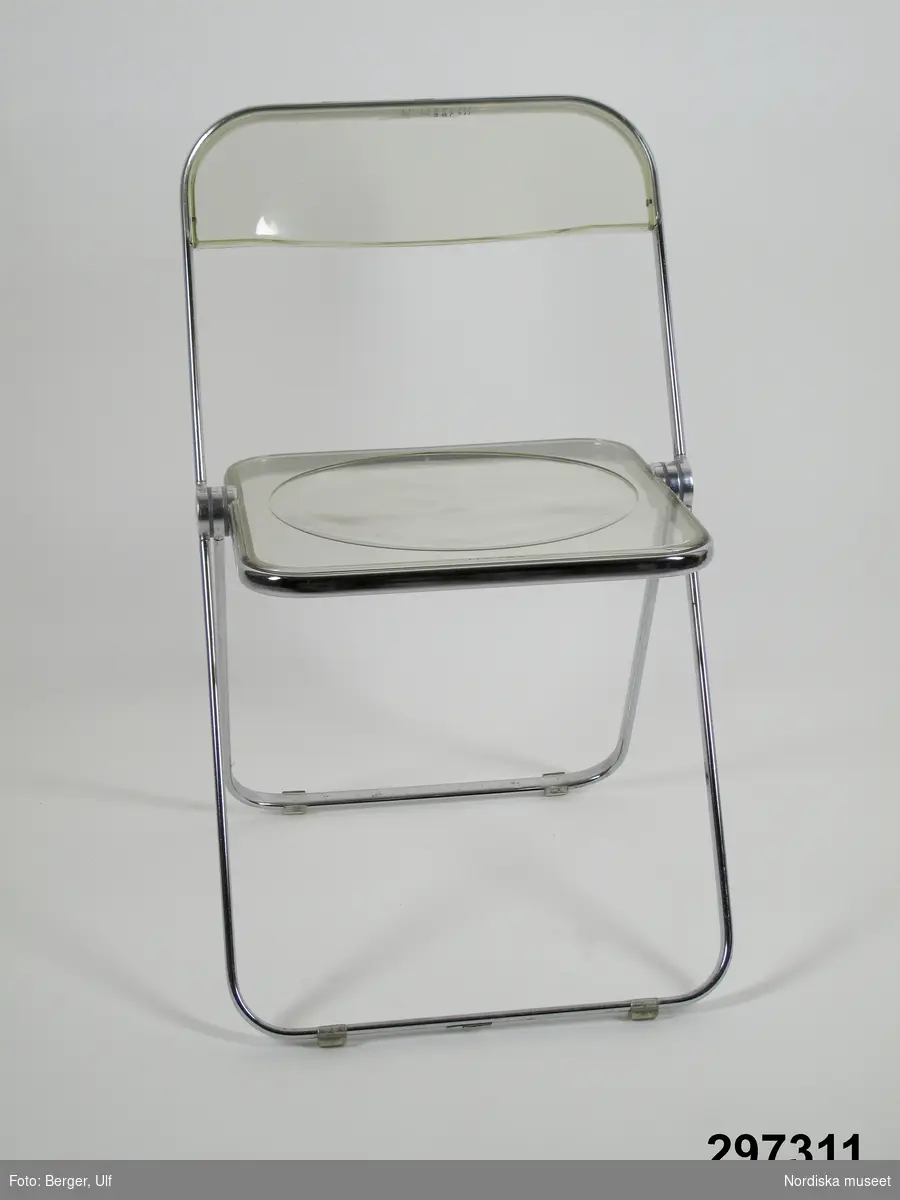 Uppgifter från katalogkort:
"Hopfällbar stol. Sitsen och ryggbrickan av formgjuten genomskinlig plast, kantad med lättmetall. Underredet av böjda lättmetallstänger.
Stolen tillverkas i en mängd färger, både i genomskinlig plast och icke genomskinlig plast. Den kan även beställas klädd med jersey i olika färger.
Tillverkningen av Plia-stolen började i slutet av 1960-talet och stolen har varit mycket populär. Den säljs genom KF och kostar 1976 ca 100 kr. I möbelhandeln kostar den 1976 ca 150-180 kronor.
Se vidare katalog i biblioteket Castelli Collection, 1973."
LG/SEN 1976
/Anna Womack 2009-06-10