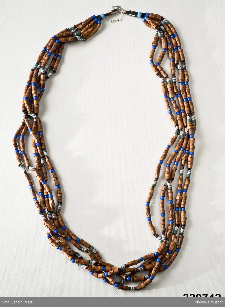 Halssmycke bestående av fem parallella halsband dekorerade med rödbruna träpärlor, blå glaspärlor samt grönvita pärlor i sten. Hake och ögla i metall. Afrikanska influenser.
/Zingoalla Rosenqvist 2009-02-05