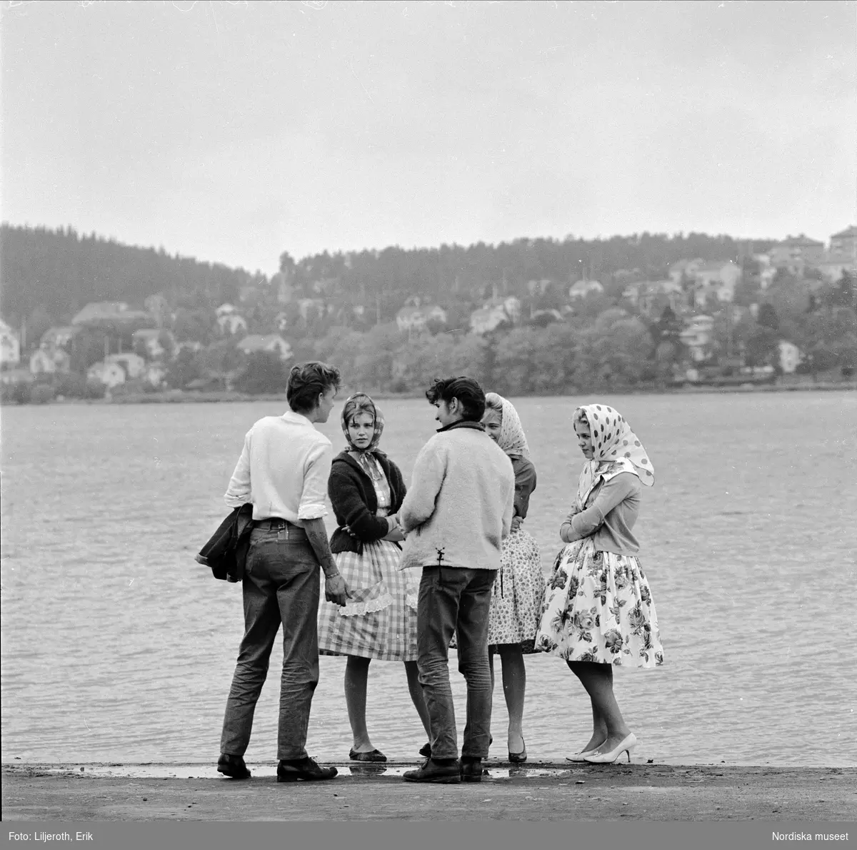 Fyra ungdomar, två pojkar och tre flickor, står och pratar vid Storsjöns strand.