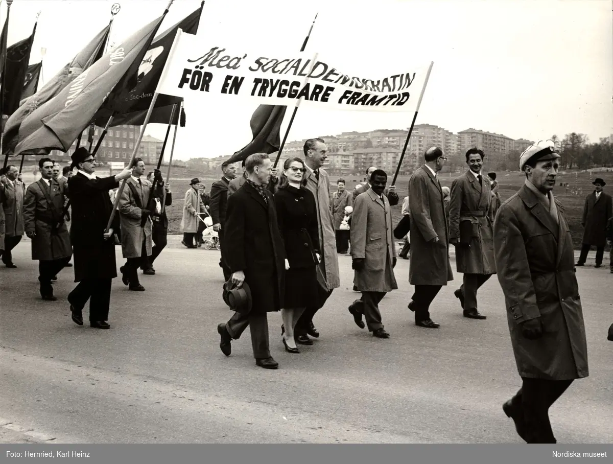 Demonstration 1:a maj. Plakat med texten "Med SOCIALDEMOKRATIN FÖR EN TRYGGARE FRAMTID". Framför plakatet går bland andra Tage Erlander, Sten Andersson, Artur Lundkvist och Maria Wine