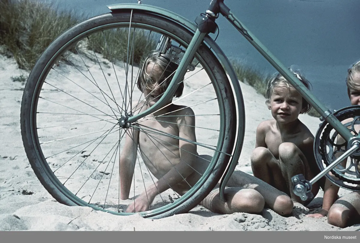 Flickor på sandstrand bakom en cykel.