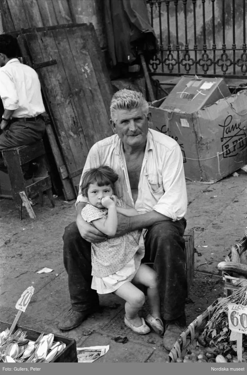 Försäljare på gata med liten flicka i knät. Italien