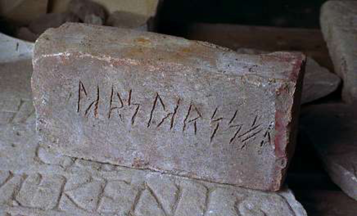 Tegelsten med 11 runor, texten LARS LARSSON, skrivet med runor och runliknande tecken. Ristningen består av 4,5 - 5 cm höga runor, som måste har ristats medan leran ännu var våt.