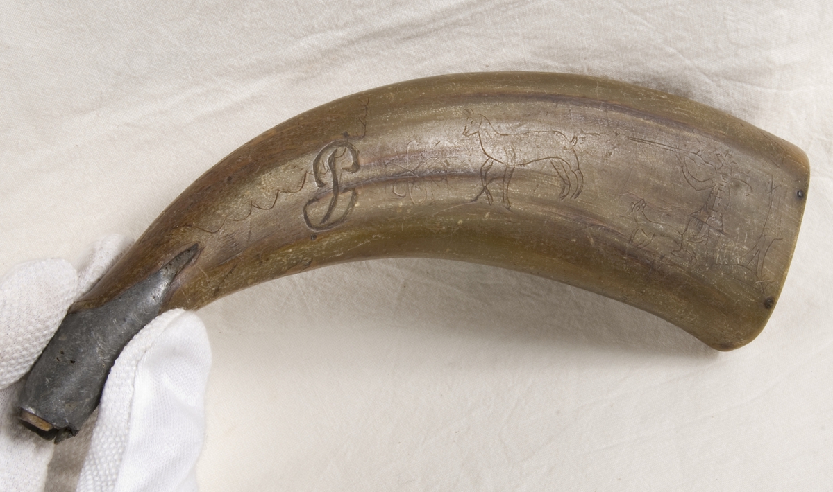 Gulgrönt horn med träbotten och tennbeslag vid mynningen. På båda sidor ristad dekor i form av jaktscener, samt namnet ANDREAS BORMAN och initialer JP. 1 [svårläst].

